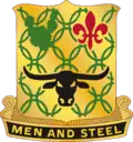 A Gold color metal and enamel device 1+1⁄8 inches (2.9 cm) in height overall consisting of a shield blazoned: Or, chain mail Vert, in chief a prickly pear cactus of the last and a fleur-de-lis Gules and in base a carabao affronté Sable. Attached below and to the sides of the shield a Black scroll turned Gold inscribed "MEN AND STEEL" in Gold letters.