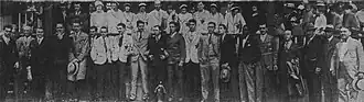 Black and white group photo of men and women dressed in formal year