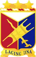 A Gold color metal and enamel device 1+1⁄4 inches (3.2 cm) consisting of a shield blazoned: Per pall Argent, Gules and Azure, over the second and third an Igorot war shield and kris in saltire Or. Attached above the shield a wreath of the colors Argent and Gules three mullets Or. Attached below the shield a Gold scroll inscribed 'LAGING UNA' in Blue letters.