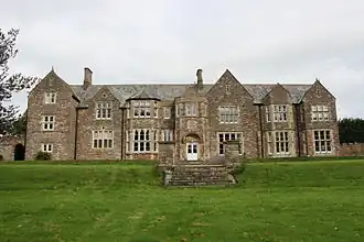 stone building with slate roof, with windows on central two bays, partly obscured by trees