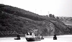 A boat passing through the opening of Barrow Bridge with 3 tug boats helping