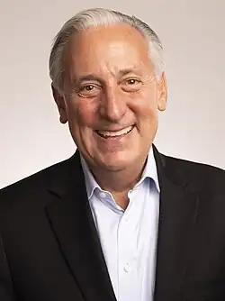 A chest-up photo of a man with white hair smiling