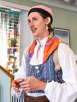 Head-and-shoulders shot of Fredy Clue. They are a tall, slender, white person with a painter's brush mustache wearing Bäckadräkten.
