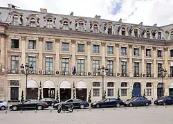 Color photograph of a building, seen slightly in profile, in the classical four-storey style. The facade features chains of refractions on the ground and mezzanine floors, as well as alternating dormers and oculi.
