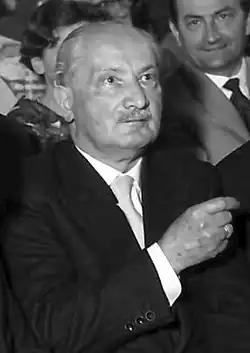 Black-and-white photo of a seated man in a dark suit with white hair.