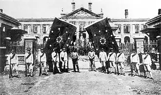A group of soldiers standing in front of a large government building, hoisting two revolutionary flags