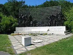 Simple sculpture of dark human figures against a fence