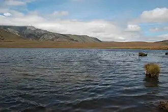 A shallow lake with rolling hills and mountains in the background