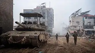 Israeli Merkava Barak with KAZ Meil Ruach and an anti-drone grille, in an urban environment during daytime