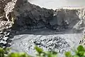 Rock cauldron containing black iron-rich mud and boiling water, with bubbling hot sulphur gas