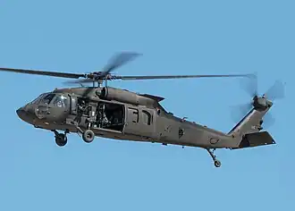A gray-black helicopter flies against a clear blue sky, with some motion blur on the rotors.