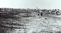In the distance a group of people walk down a dirt road away from the village.