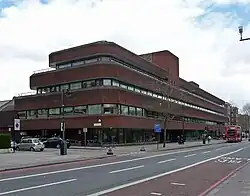 Exterior of large three storey red brick and glass building next to road