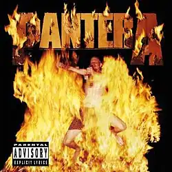 A shirtless man jumping through fire while holding a bottle of whiskey.