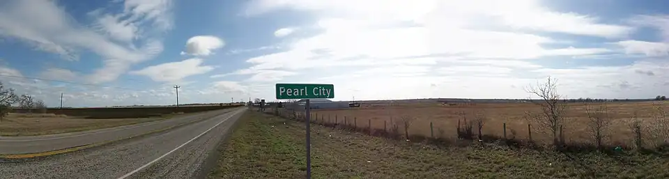 A rural road with the Pearl City sign in the foreground. A few small buildings are barely visible in the distance.