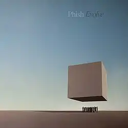 A group of people stand under a large, floating cube in an empty landscape.