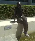 Susanne (2005), life-sized bronze nude, sits on a wall beside a reflecting pond, BBP.