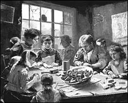 People of various ages sit around a table engaged in handiwork.