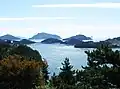 A clear bright ocean sparkling with light, dotted with several small forested islands.