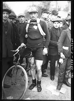 A man posing with a bike while wearing a hat.